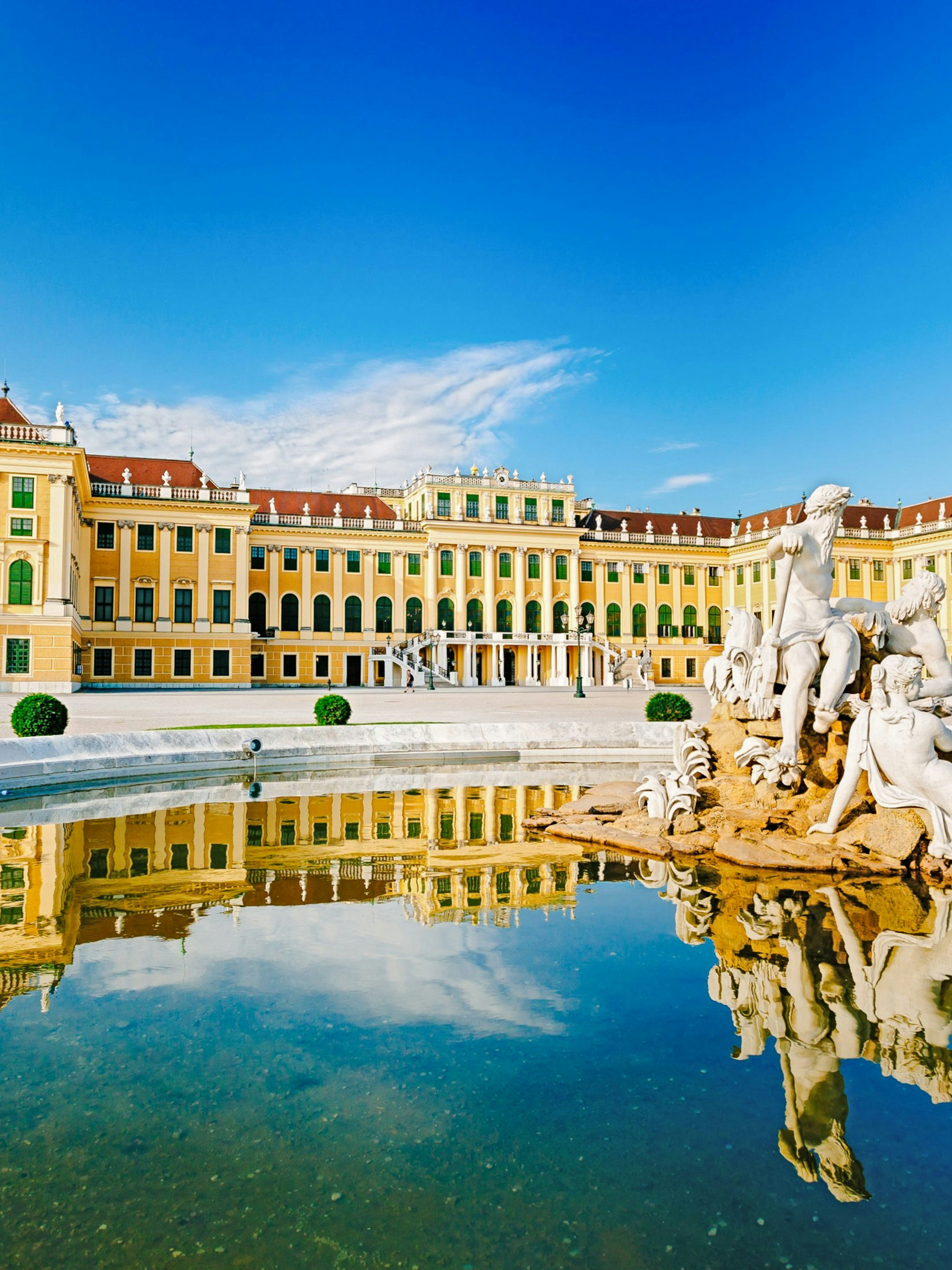 Schonbrunn Palace in Vienna with Neptune Fountain reflecting in the foreground.