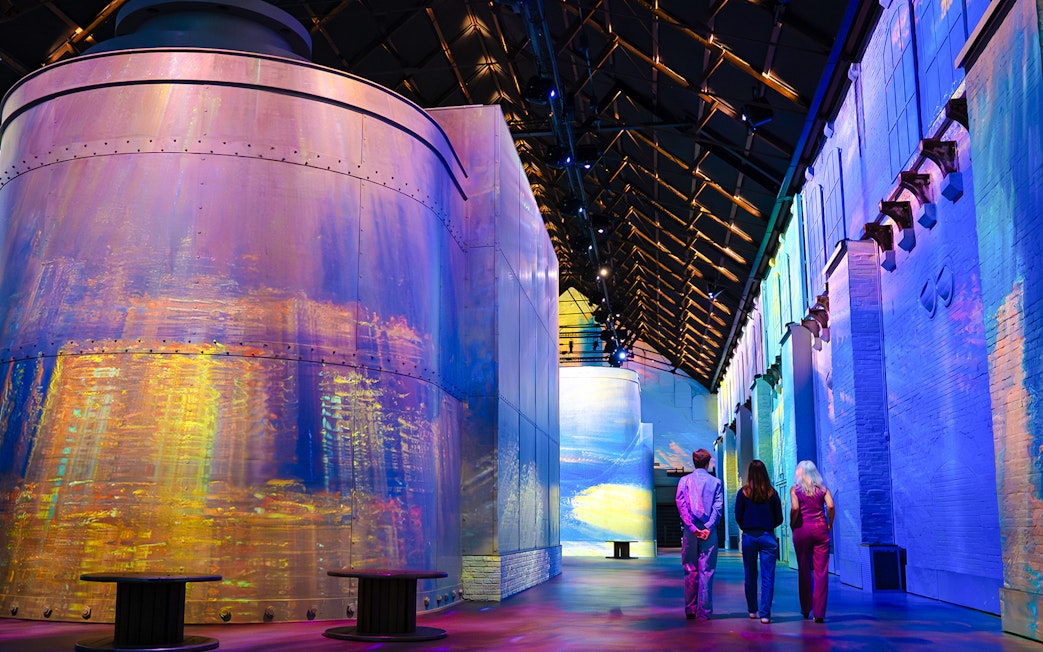 Visitors at Monet exhibition in Fabrique des Lumières, surrounded by colorful projections.
