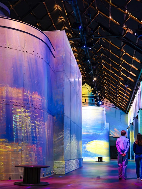 Visitors at Monet exhibition in Fabrique des Lumières, surrounded by colorful projections.