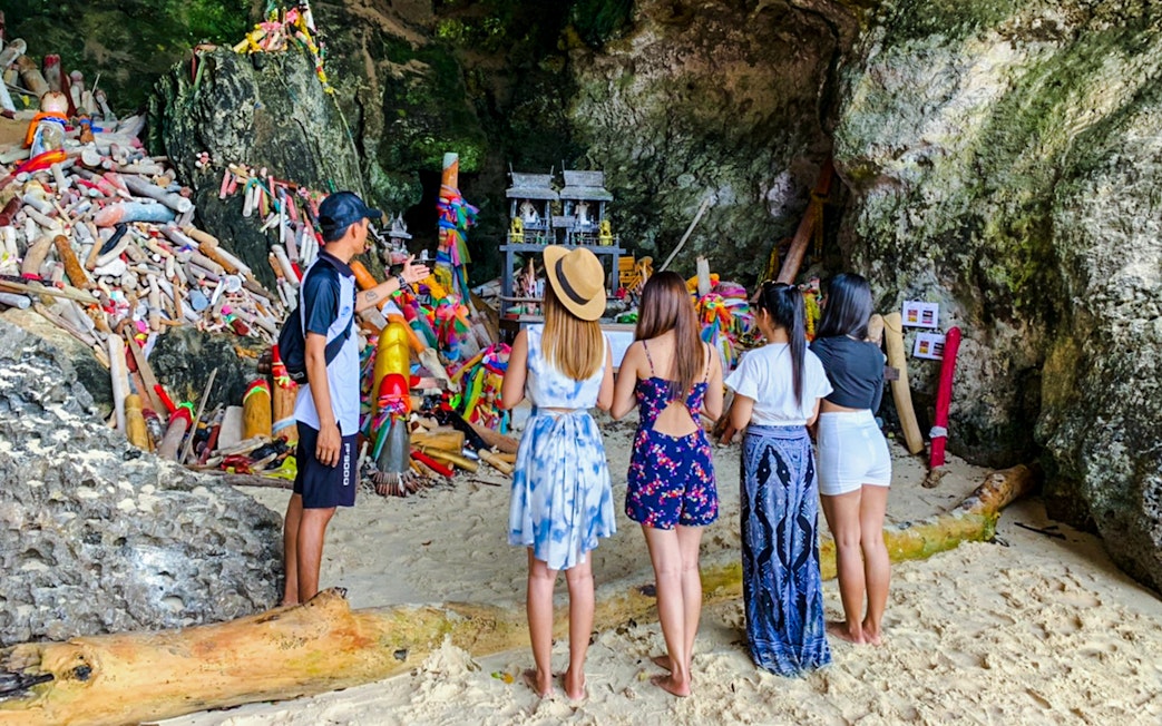 Tourists at Phranang Cave Beach in Krabi, Thailand, observing a shrine with colorful offerings.