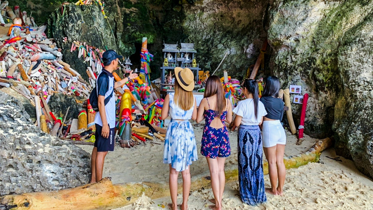 Tourists at Phranang Cave Beach in Krabi, Thailand, observing a shrine with colorful offerings.
