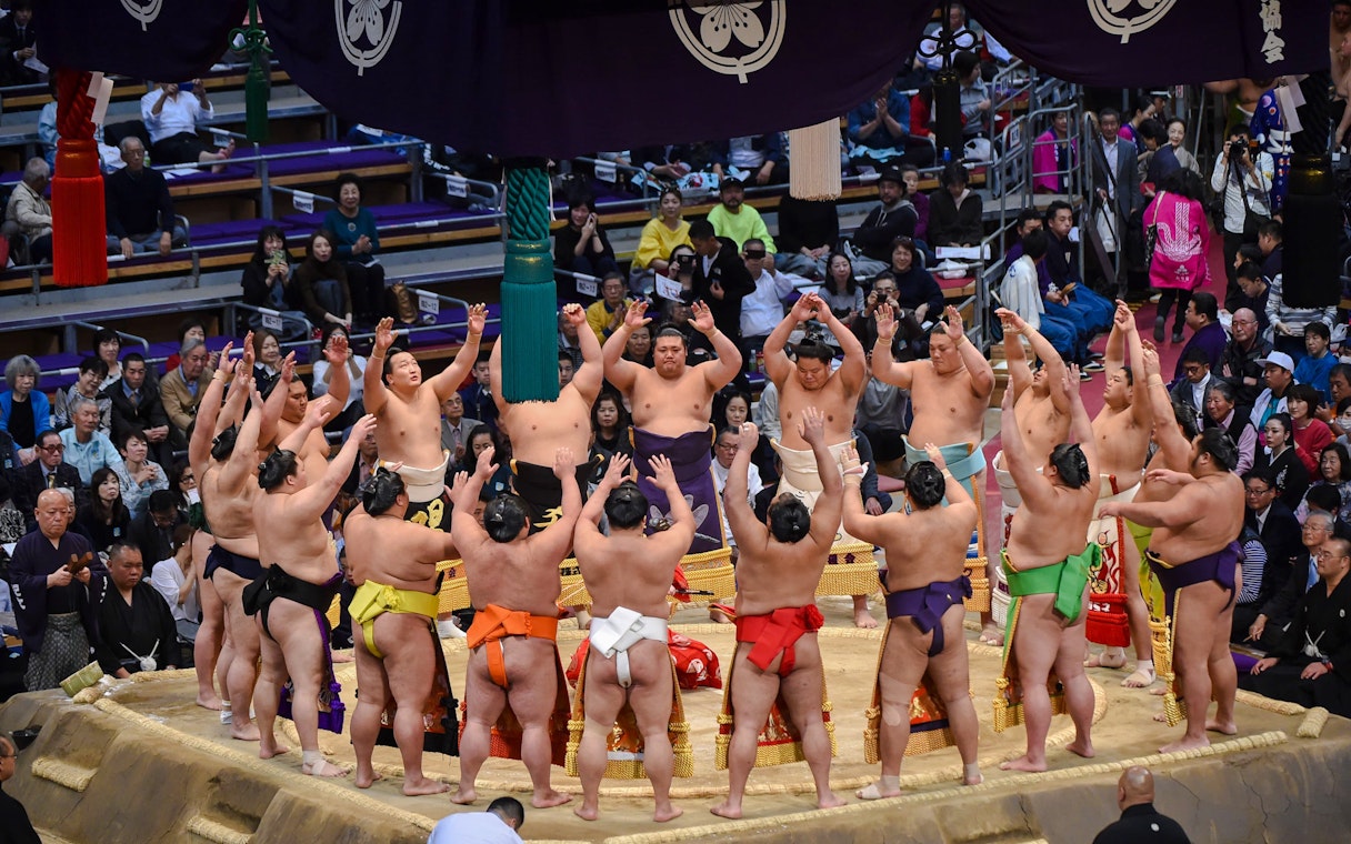 Sumo wrestlers perform a pre-tournament ceremony in a crowded arena in Japan.