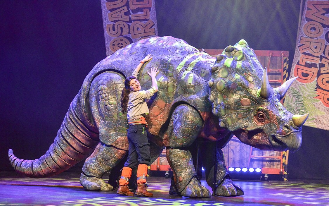 Performer with dinosaur puppet on stage at Dinosaur World Live, Westend.