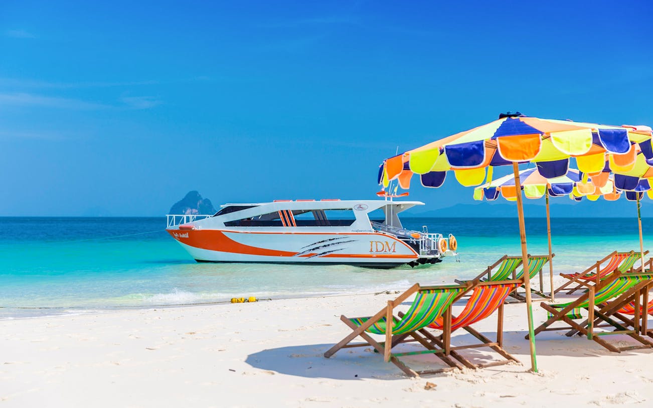 Speed catamaran near colorful beach chairs and umbrellas on Phuket's sandy shore.