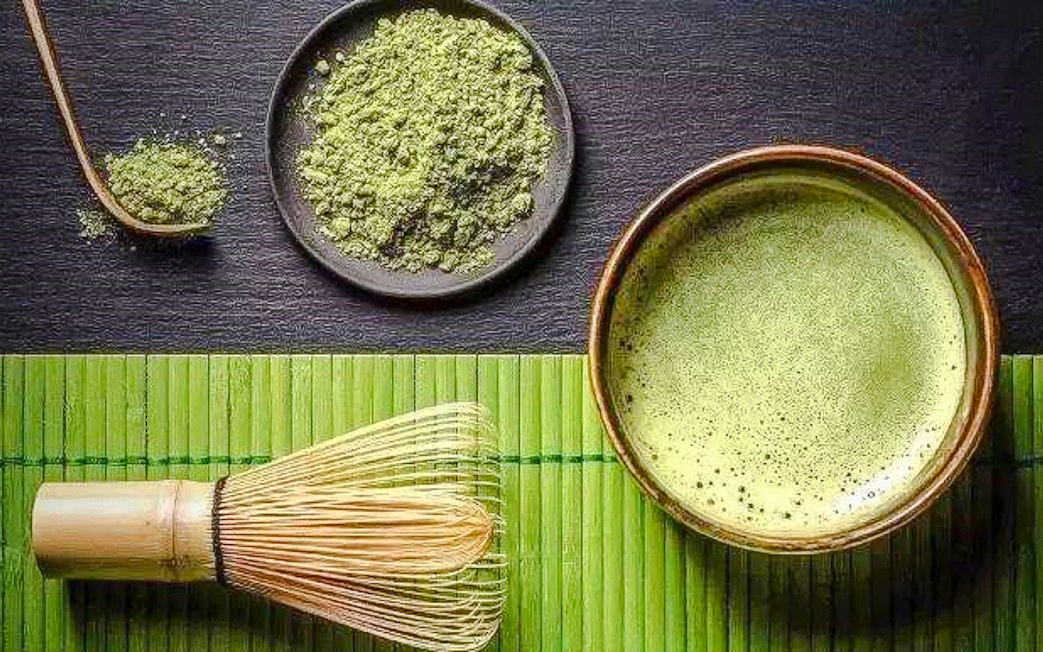 Bamboo whisk, matcha bowl, and powder on a bamboo mat.