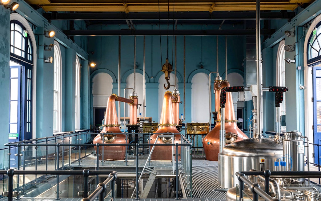 Copper stills inside Titanic Whiskey Distillery with arched windows and industrial equipment.