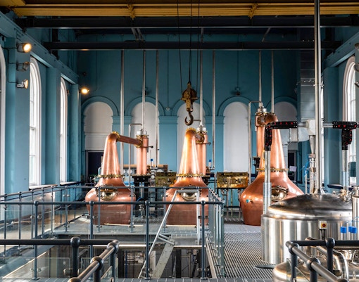 Copper stills inside Titanic Whiskey Distillery with arched windows and industrial equipment.