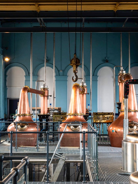 Copper stills inside Titanic Whiskey Distillery with arched windows and industrial equipment.