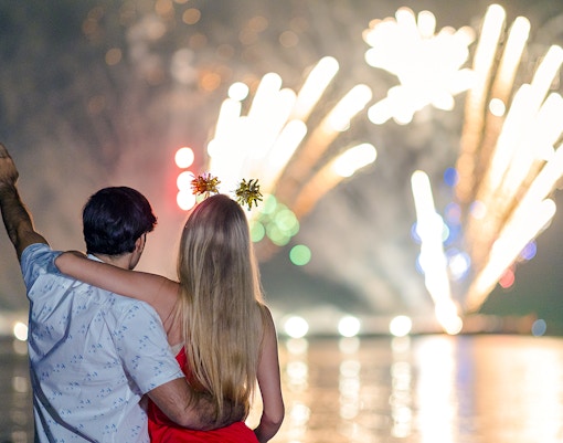 Young couple watching fireworks over water at night.