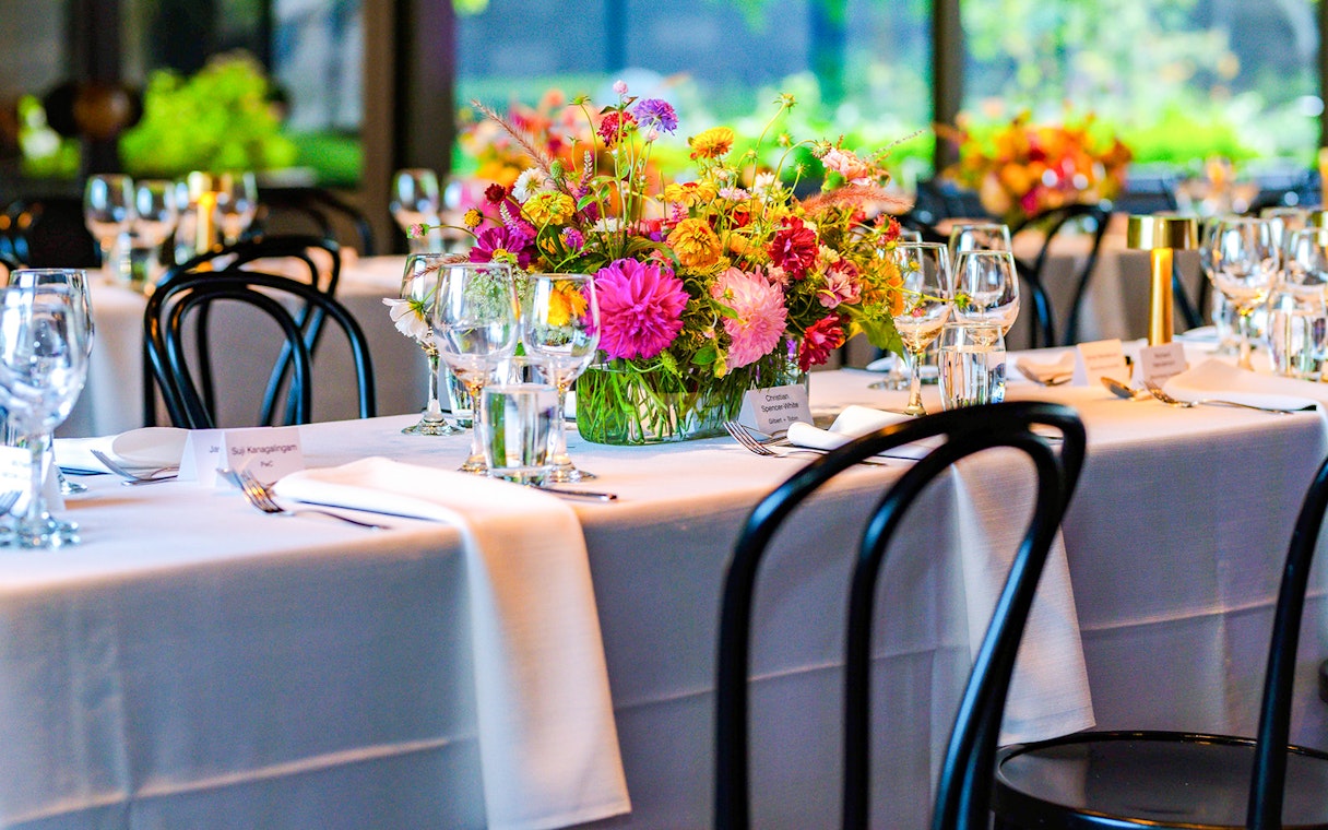 NGV garden restaurant interior with tables set and floral centerpieces.