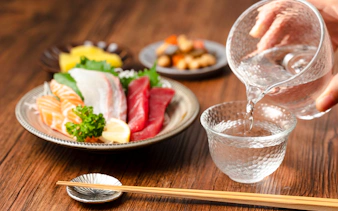 Sashimi platter with sake being poured into a glass, featuring salmon and tuna slices.
