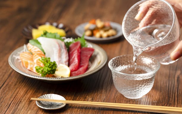 Sashimi platter with sake being poured into a glass, featuring salmon and tuna slices.