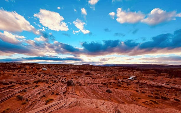 Horseshoe Bend desert landscape with vehicles on a trail under a vibrant sky.
