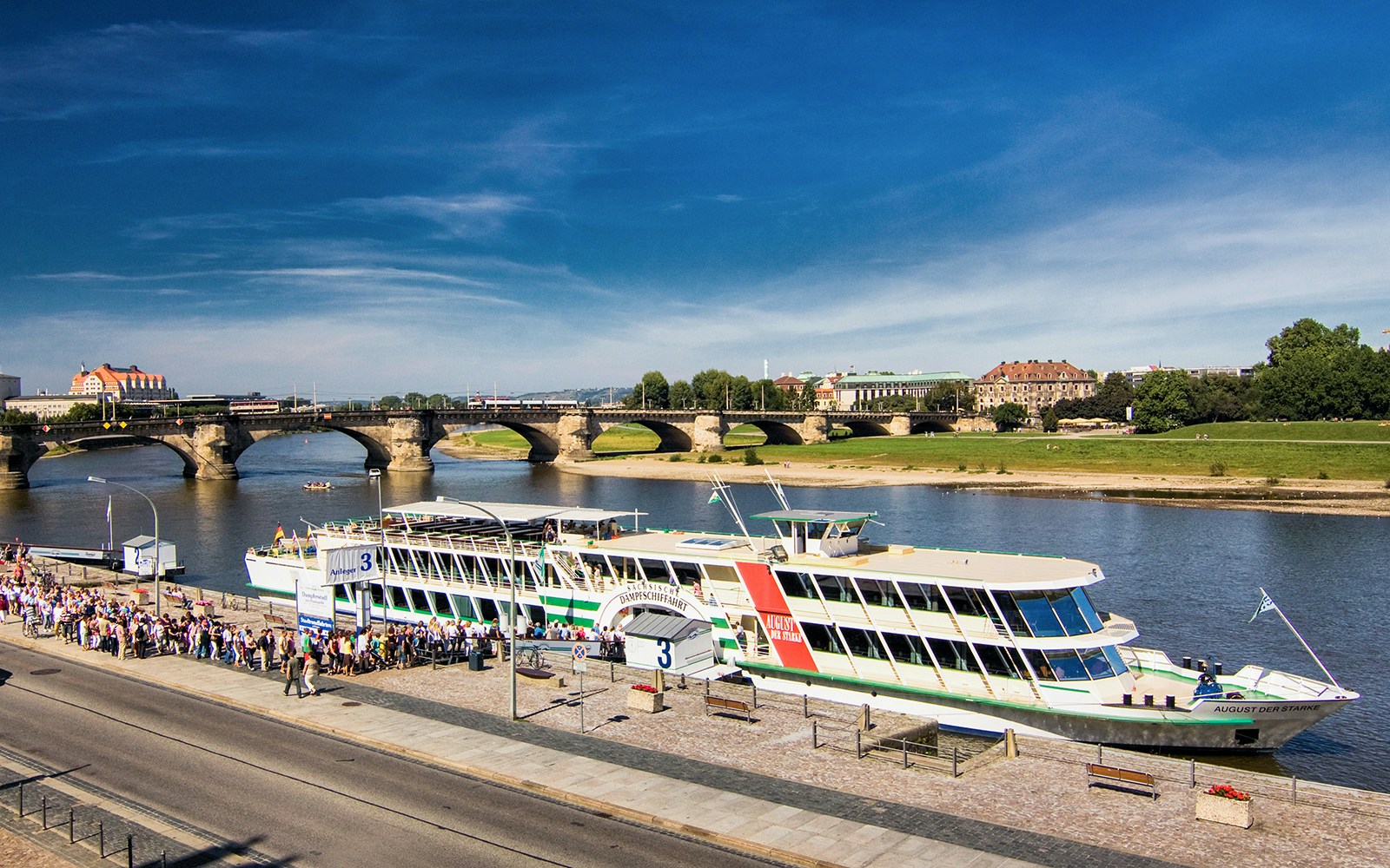 Elbe River cruise ship docked with passengers boarding, Dresden bridge in background.