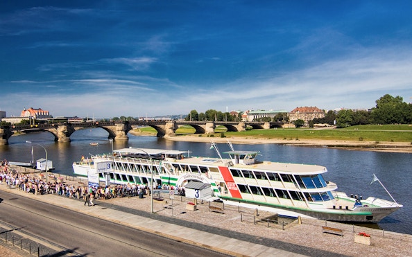 Elbe River cruise ship docked with passengers boarding, Dresden bridge in background.
