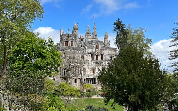 Quinta da Regaleira in Sintra surrounded by lush greenery and blue sky.
