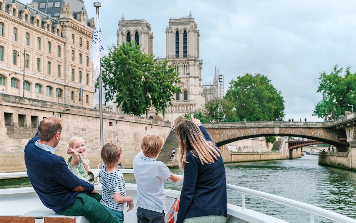 Family enjoying a Seine River cruise with a view of Notre-Dame Cathedral in Paris.