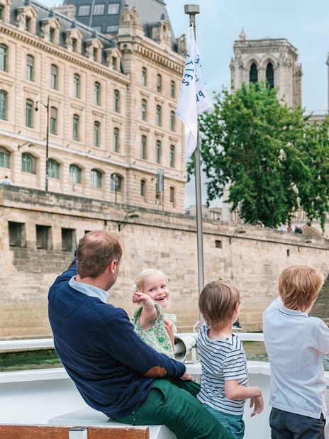 Family enjoying a Seine River cruise with a view of Notre-Dame Cathedral in Paris.