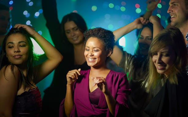 Women dancing joyfully at a lively party with colorful lights.