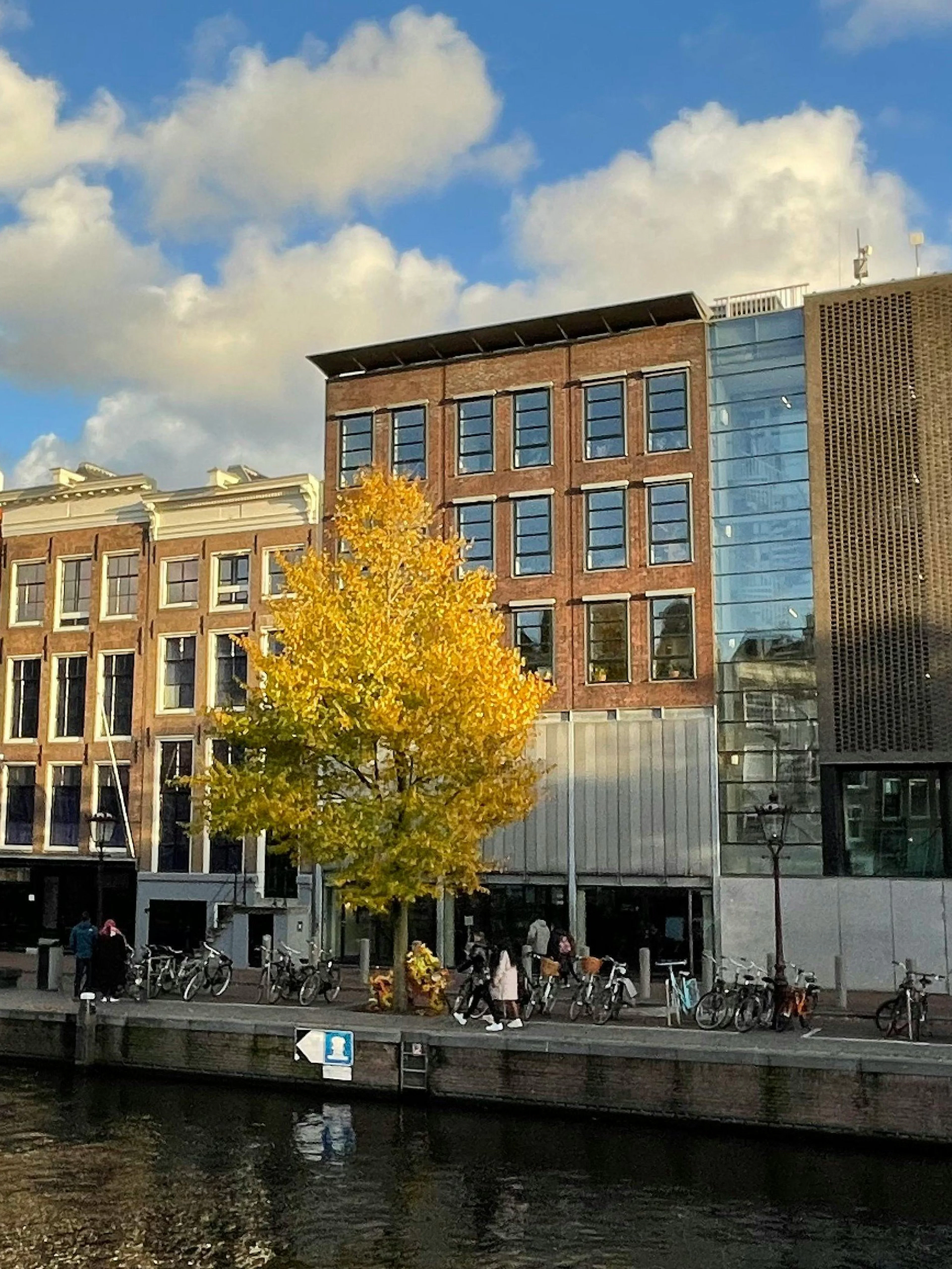 Anne Frank House along Amsterdam canal with autumn trees and tour boat.