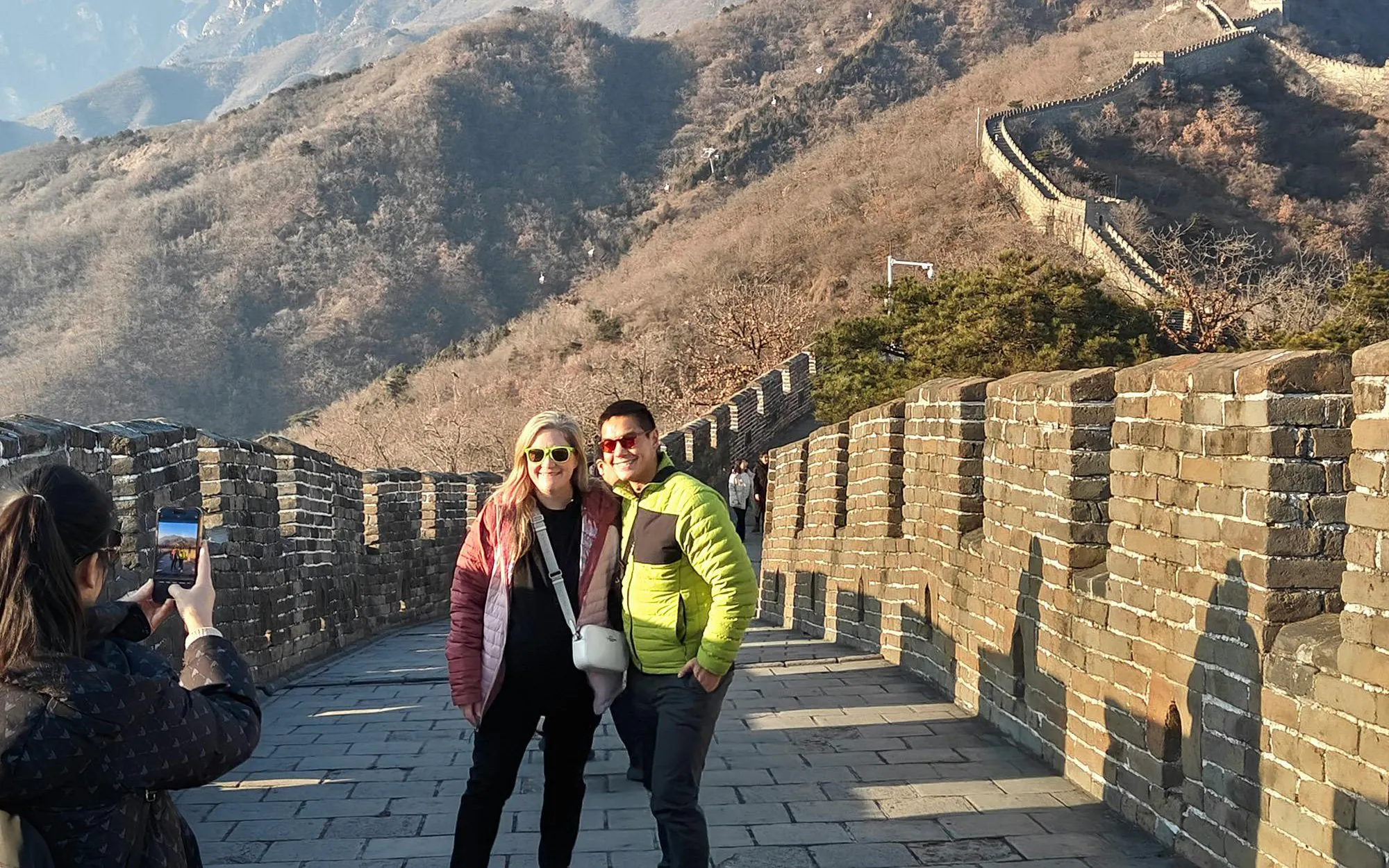 Tourists posing on Mutianyu section of the Great Wall, China, with scenic mountain backdrop.