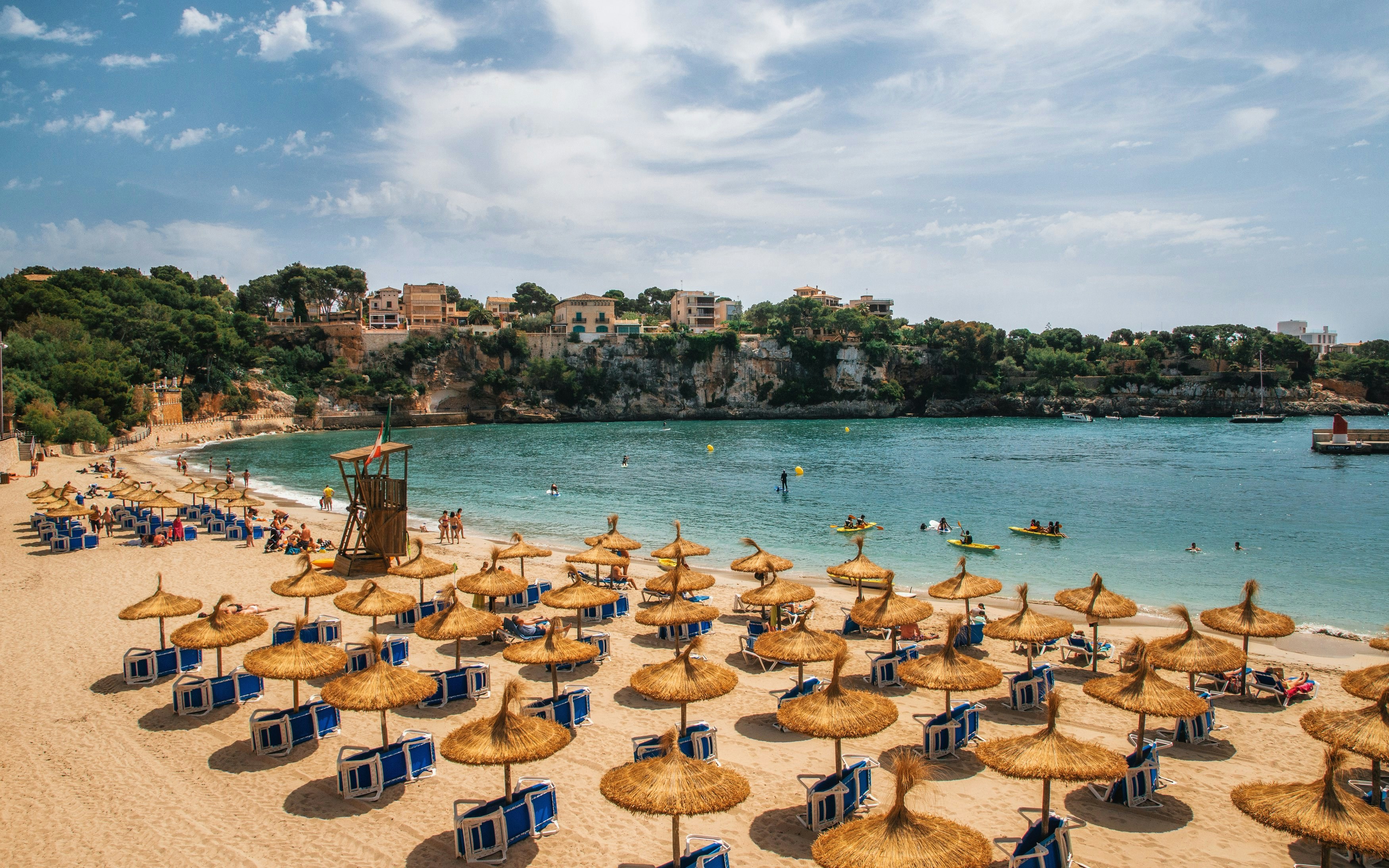 Beach with straw umbrellas and sun loungers in Porto Cristo, Mallorca, Spain.