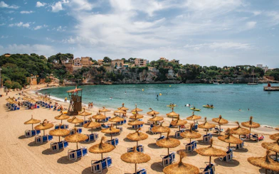 Beach with straw umbrellas and sun loungers in Porto Cristo, Mallorca, Spain.
