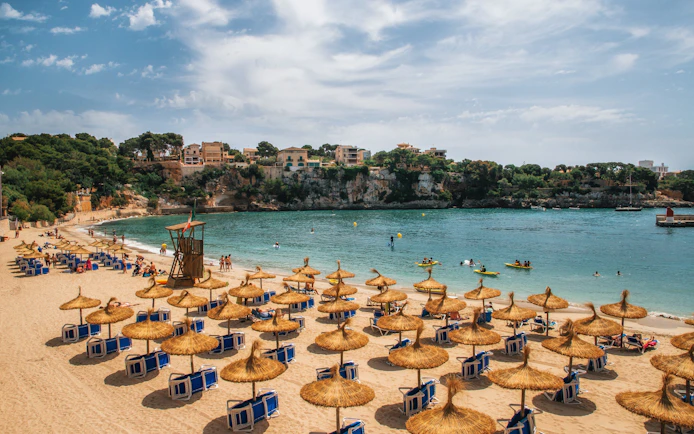 Beach with straw umbrellas and sun loungers in Porto Cristo, Mallorca, Spain.