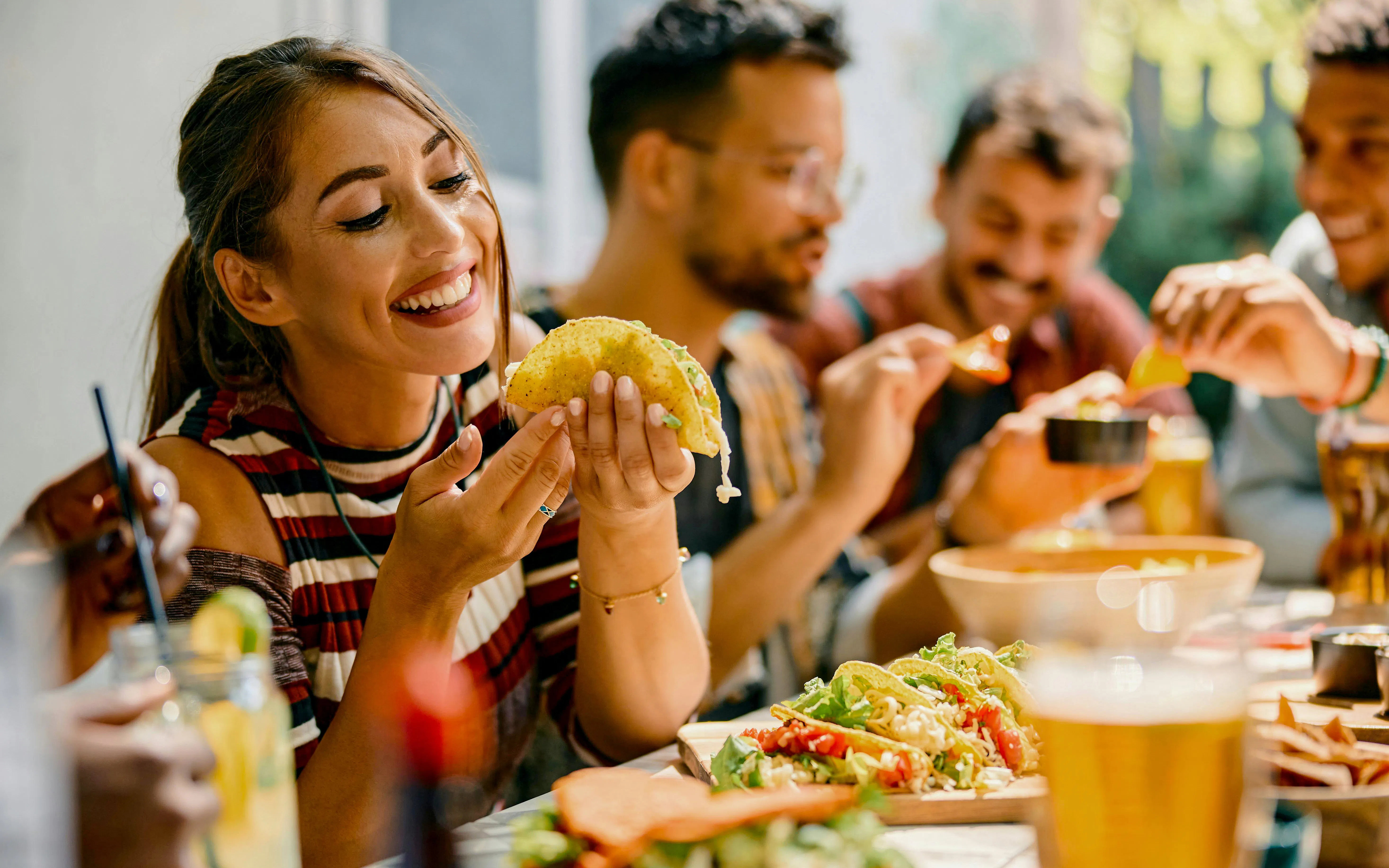 Friends enjoying tacos and drinks at an outdoor lunch gathering.