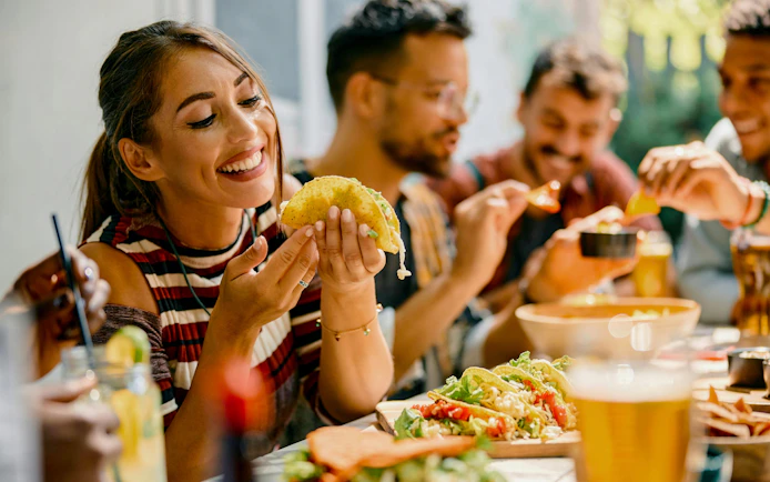 Friends enjoying tacos and drinks at an outdoor lunch gathering.
