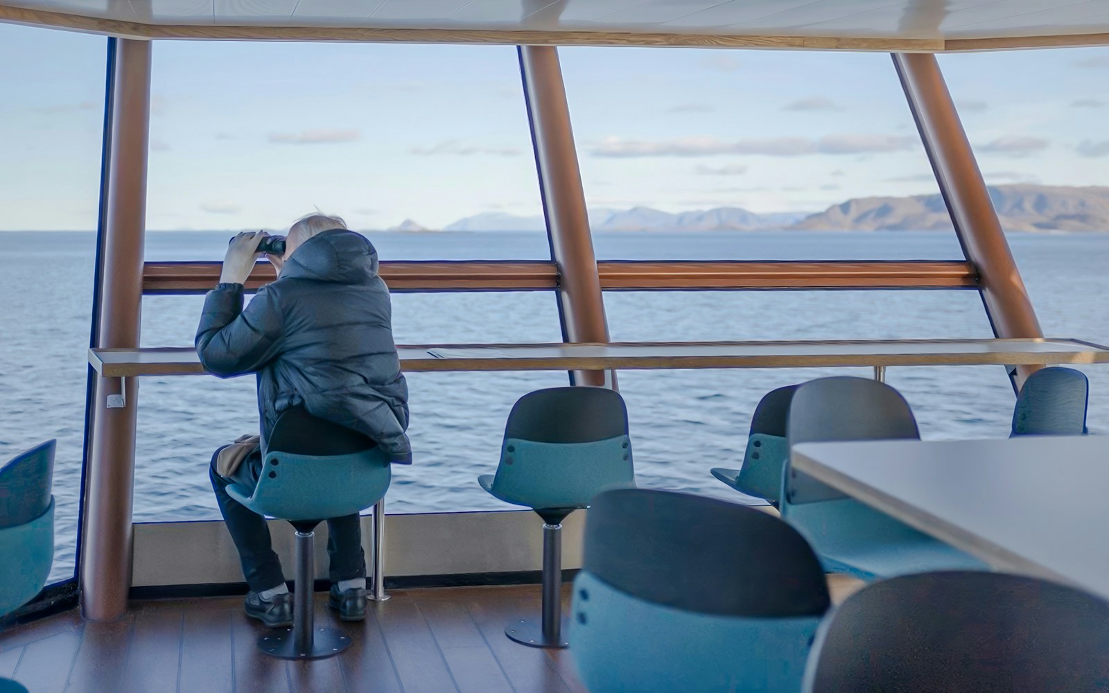 Cruise passenger viewing Lofoten landscape through panoramic windows on Silent Trollfjord Cruise.