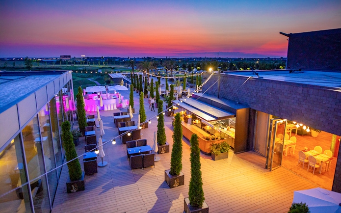 Rooftop terrace at Therme Bucuresti during sunset with dining area and string lights.