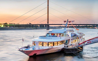 Cruise ship on the Rhine River at sunset with Düsseldorf bridge in the background.