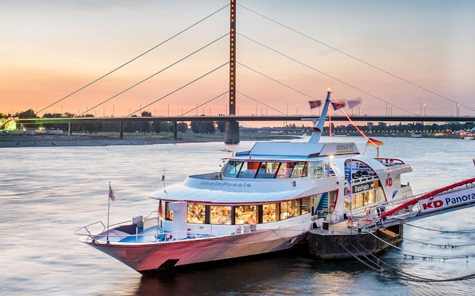 Cruise ship on the Rhine River at sunset with Düsseldorf bridge in the background.