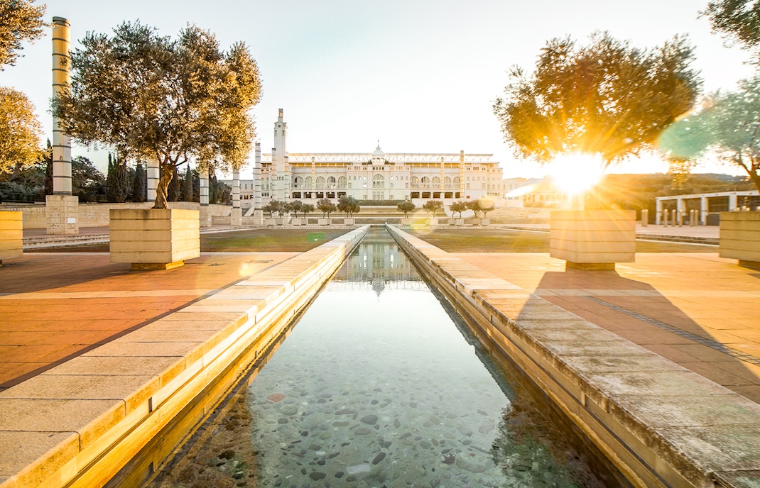 Olympic Stadium in Montjuic, Barcelona, Spain, with surrounding greenery and clear blue sky.