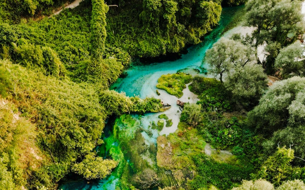 Aerial view of The Blue Eye of Theth, Albania, surrounded by lush greenery and turquoise water.