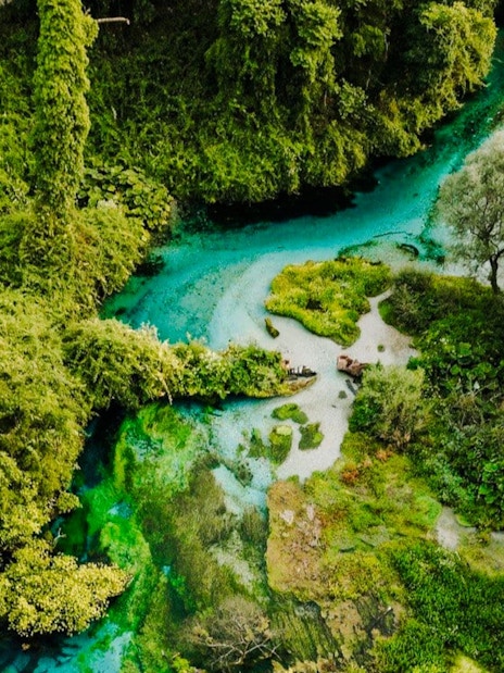 Aerial view of The Blue Eye of Theth, Albania, surrounded by lush greenery and turquoise water.