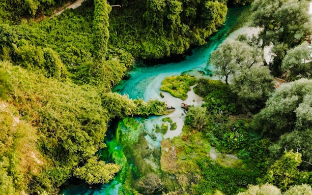 Aerial view of The Blue Eye of Theth, Albania, surrounded by lush greenery and turquoise water.