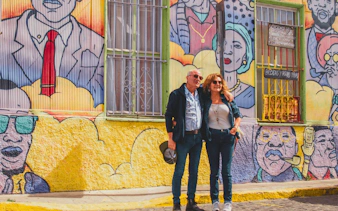 Couple standing in front of colorful mural in Valparaíso, Chile, featuring vibrant street art.