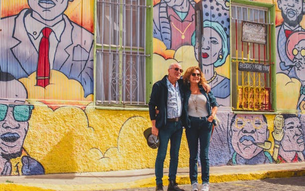 Couple standing in front of colorful mural in Valparaíso, Chile, featuring vibrant street art.
