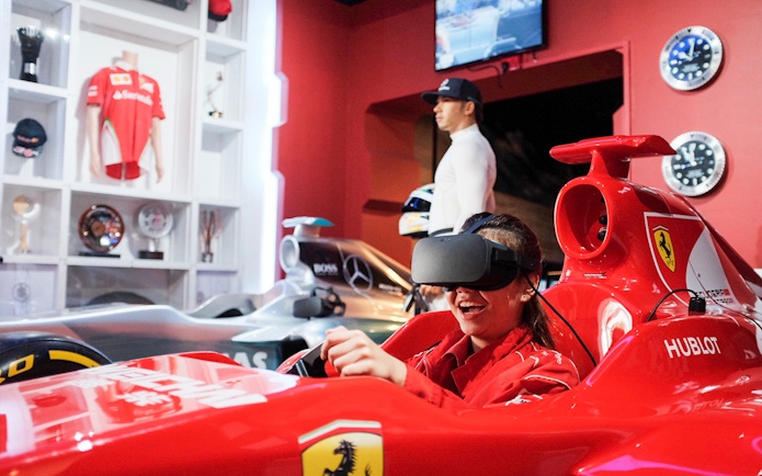Visitor enjoying a VR racing experience at Madame Tussauds Singapore with wax figure in background.
