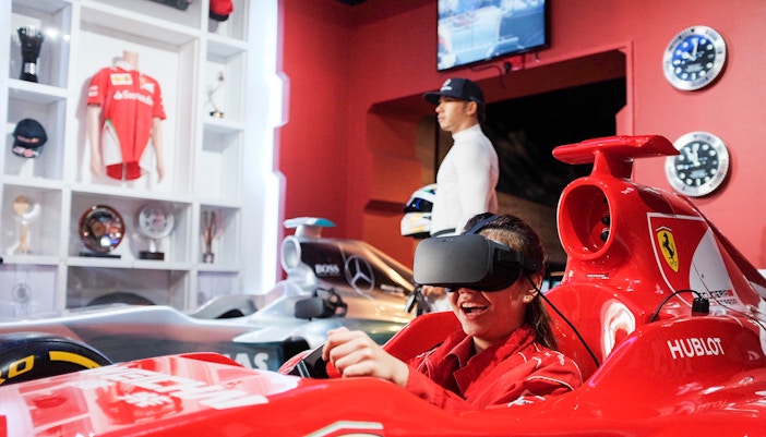 Visitor enjoying a VR racing experience at Madame Tussauds Singapore with wax figure in background.