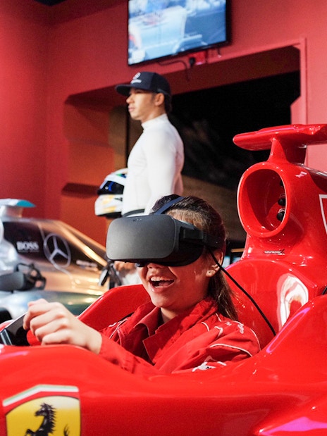 Visitor enjoying a VR racing experience at Madame Tussauds Singapore with wax figure in background.