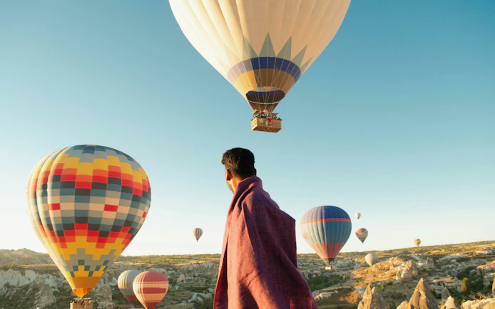 Hot air balloons over Cappadocia landscape at sunrise, person watching.