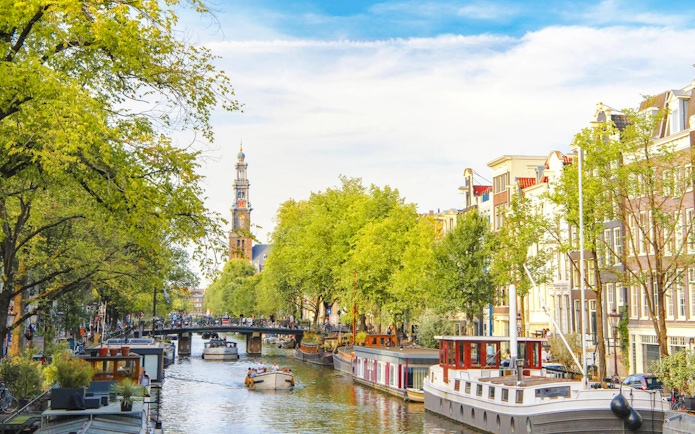 Canal view with boats and Westerkerk tower in Amsterdam Red Light District.