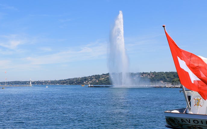 Jet d'Eau fountain on Lake Geneva with Swiss flag in foreground.