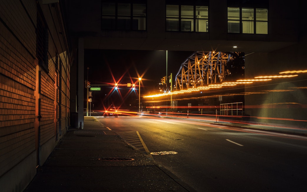 Downtown Charleston street at night with light trails and bridge in view.