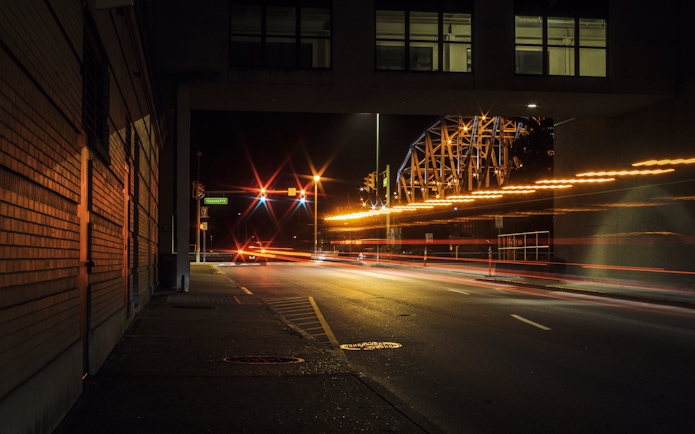 Downtown Charleston street at night with light trails and bridge in view.
