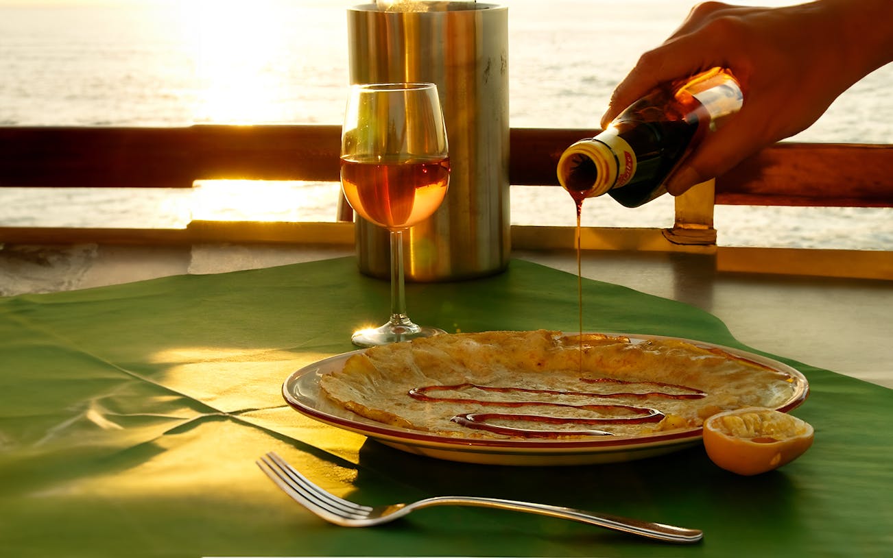 Pancake with syrup and wine on a table during an Amsterdam cruise at sunset.