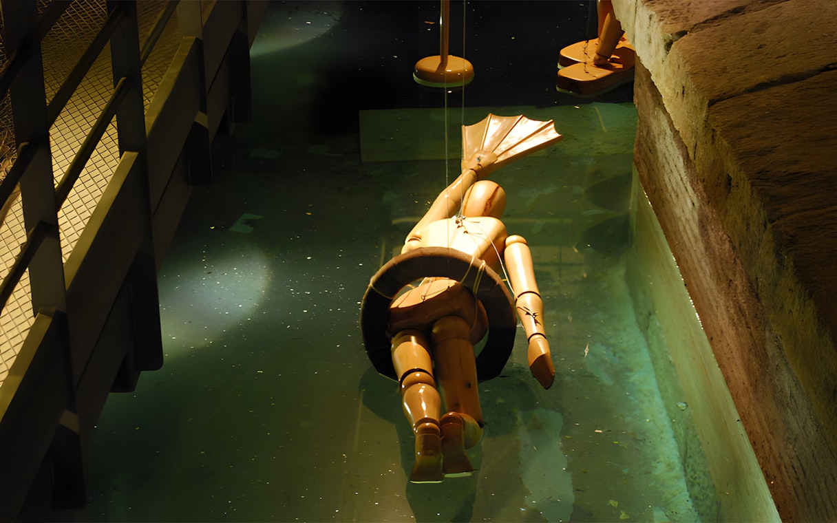 Wooden diving suit model in water at Leonardo da Vinci Museum exhibit.